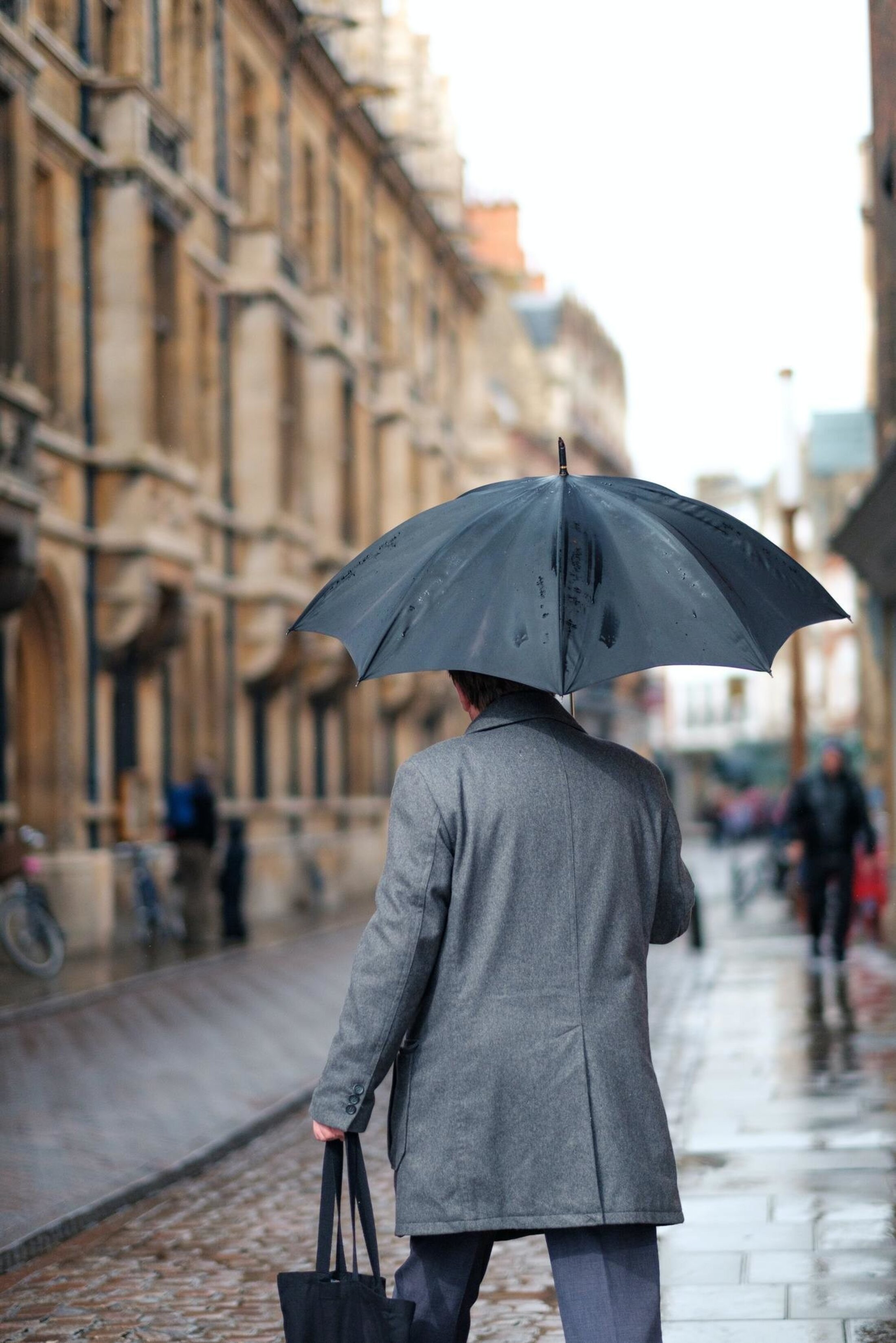 Person with a black umbrella walking along a rainy urban street.