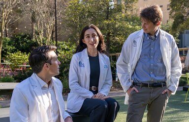 Three young people in white medical coats hang out in an outdoor gathering space.