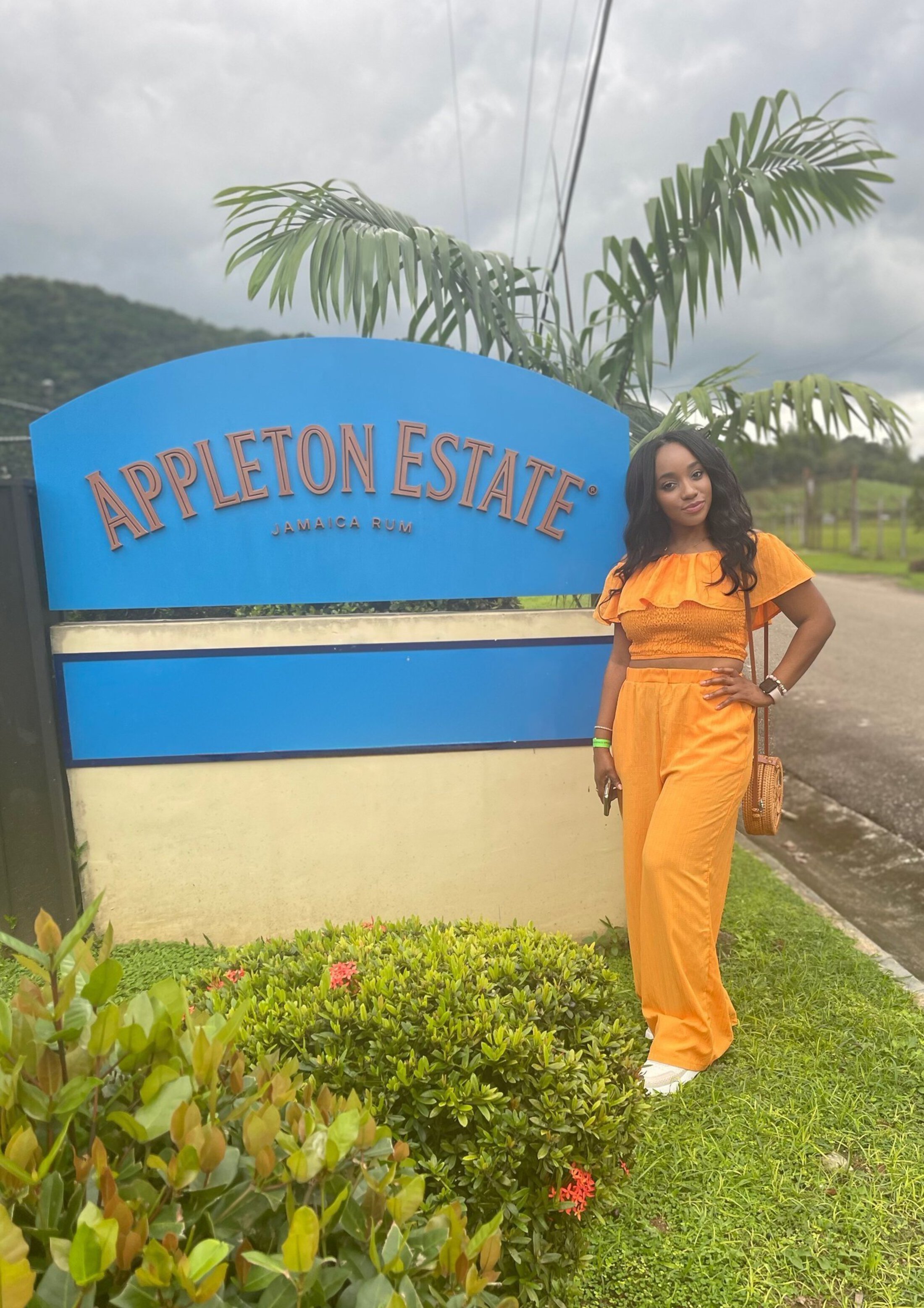 Jamaica story Tania Thomas with Appleton Estate sign wearing an yellow orange outfit