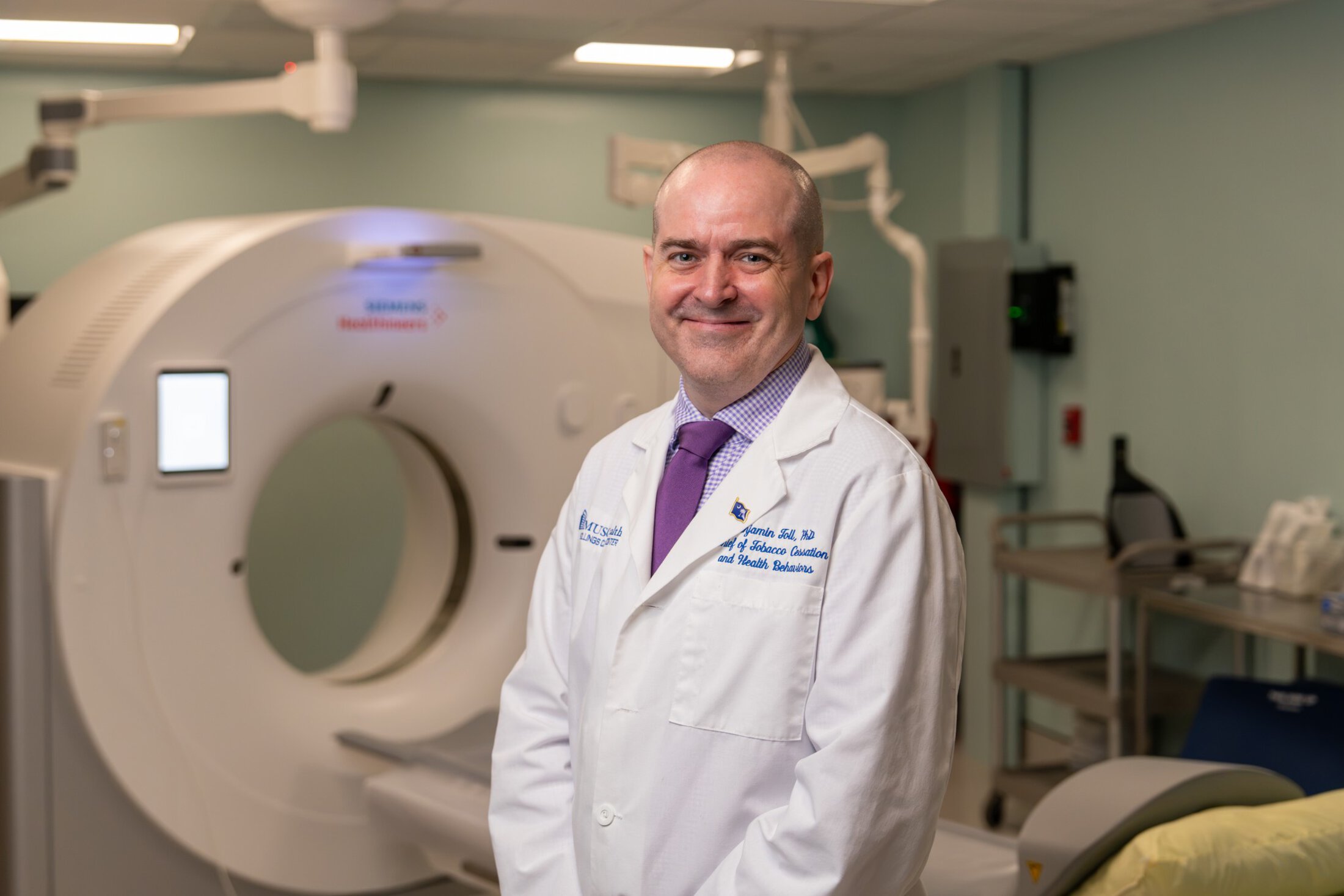 A psychologist in white lab coat stands in front of a CT scanner.