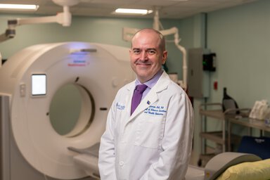 A psychologist in white lab coat stands in front of a CT scanner.