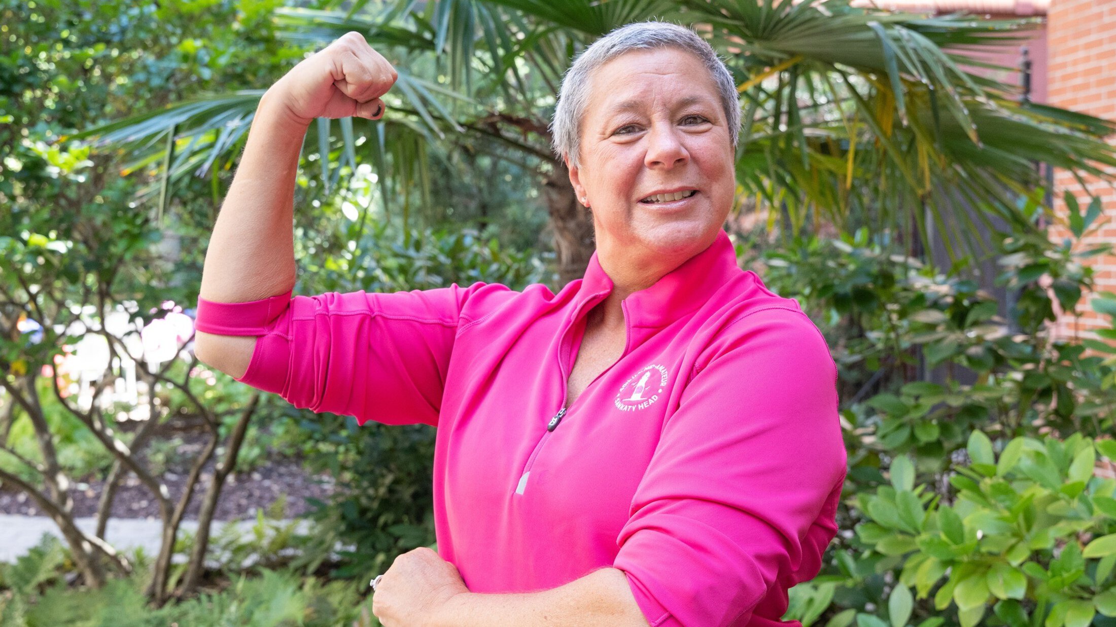 headshot of Joannah Sampson in a pink top flexing her right arm