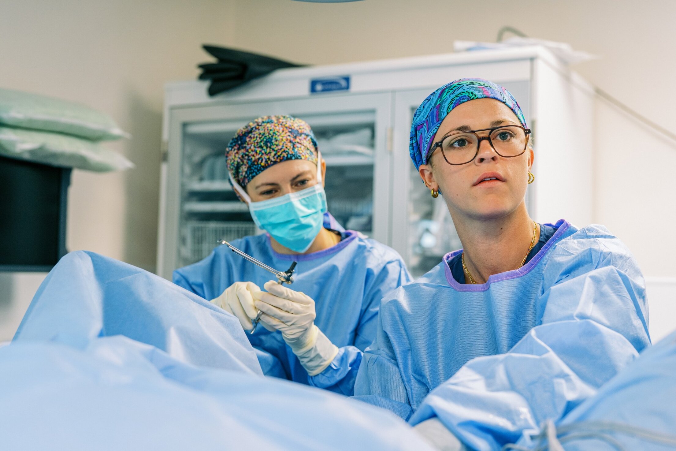 A Urology Resident carefully performs a procedure, with support from another doctor.