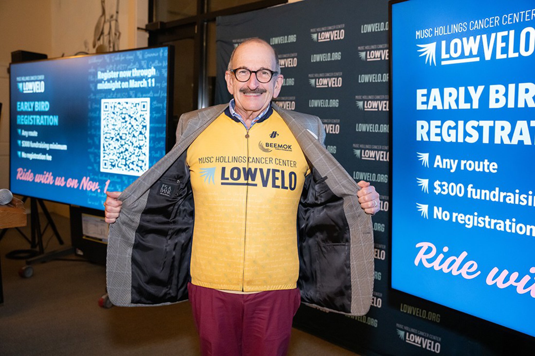 A man pulls open his blazer to reveal he's wearing a gold cycling jersey for LOWVELO.