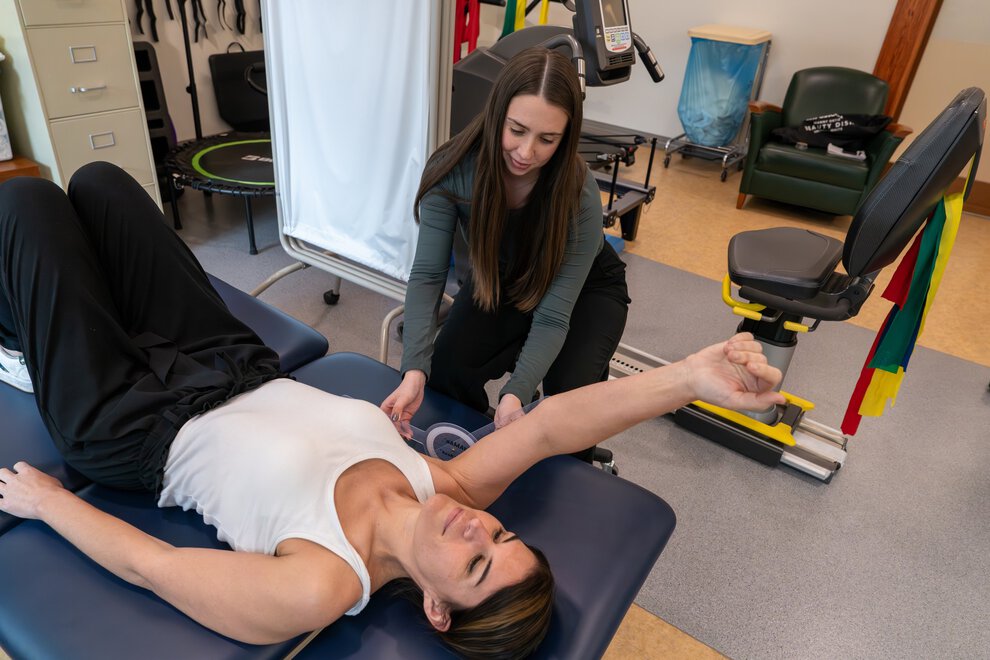 a woman uses an angle measurement tool to judge how far another woman can raise her arm above her shoulder