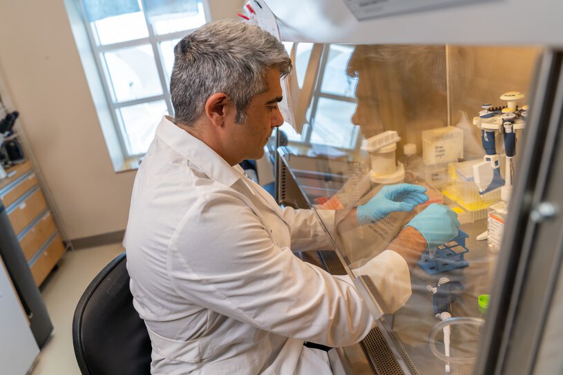 Aguirre De Cubas wears gloves while working with his hands under a hood.