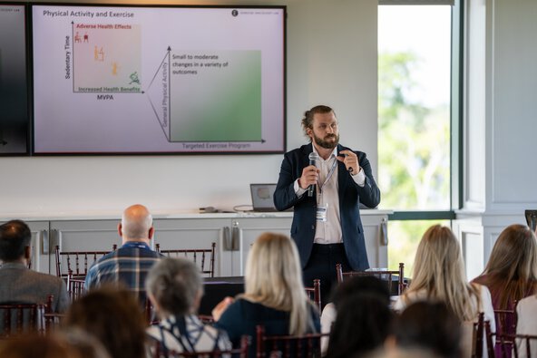 A man gestures with his hand to indicate the size of something while speaking to a room full of people.