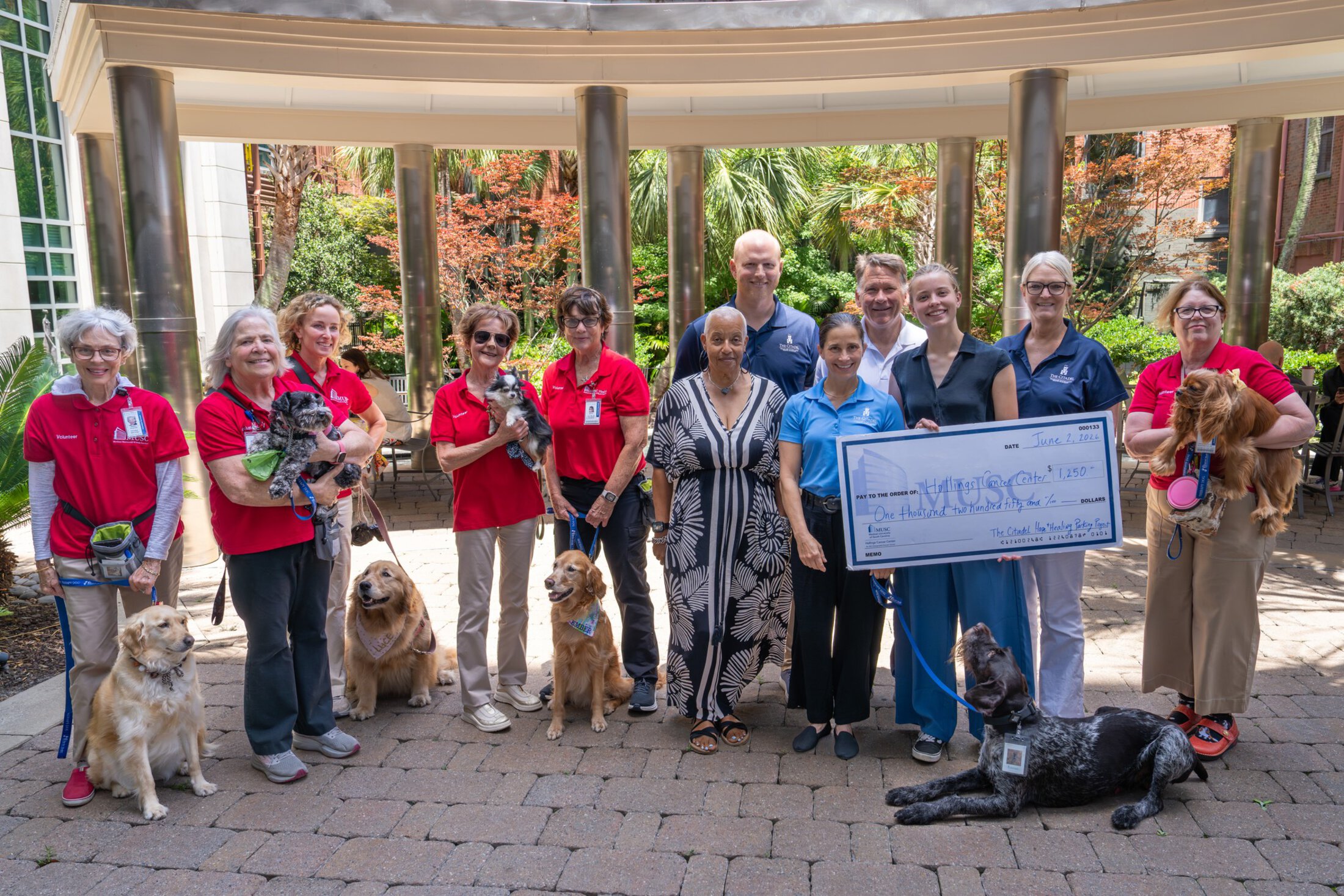 A large group of people and dogs gather around an oversized check made out for $1250.