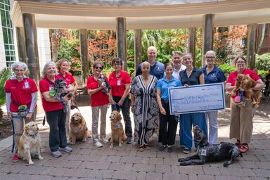 A large group of people and dogs gather around an oversized check made out for $1250.