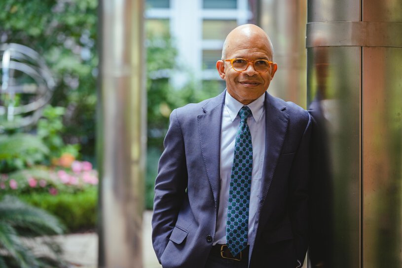 Craig Lockhart in suit and tie leans against a pillar in the garden.