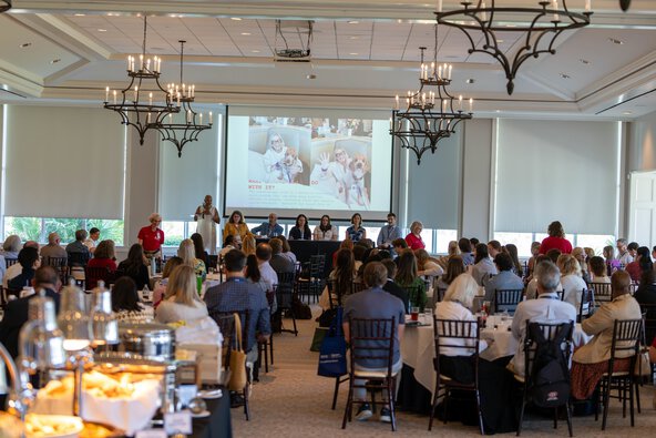 A large room of people seated at tables listen to a panel discussion.