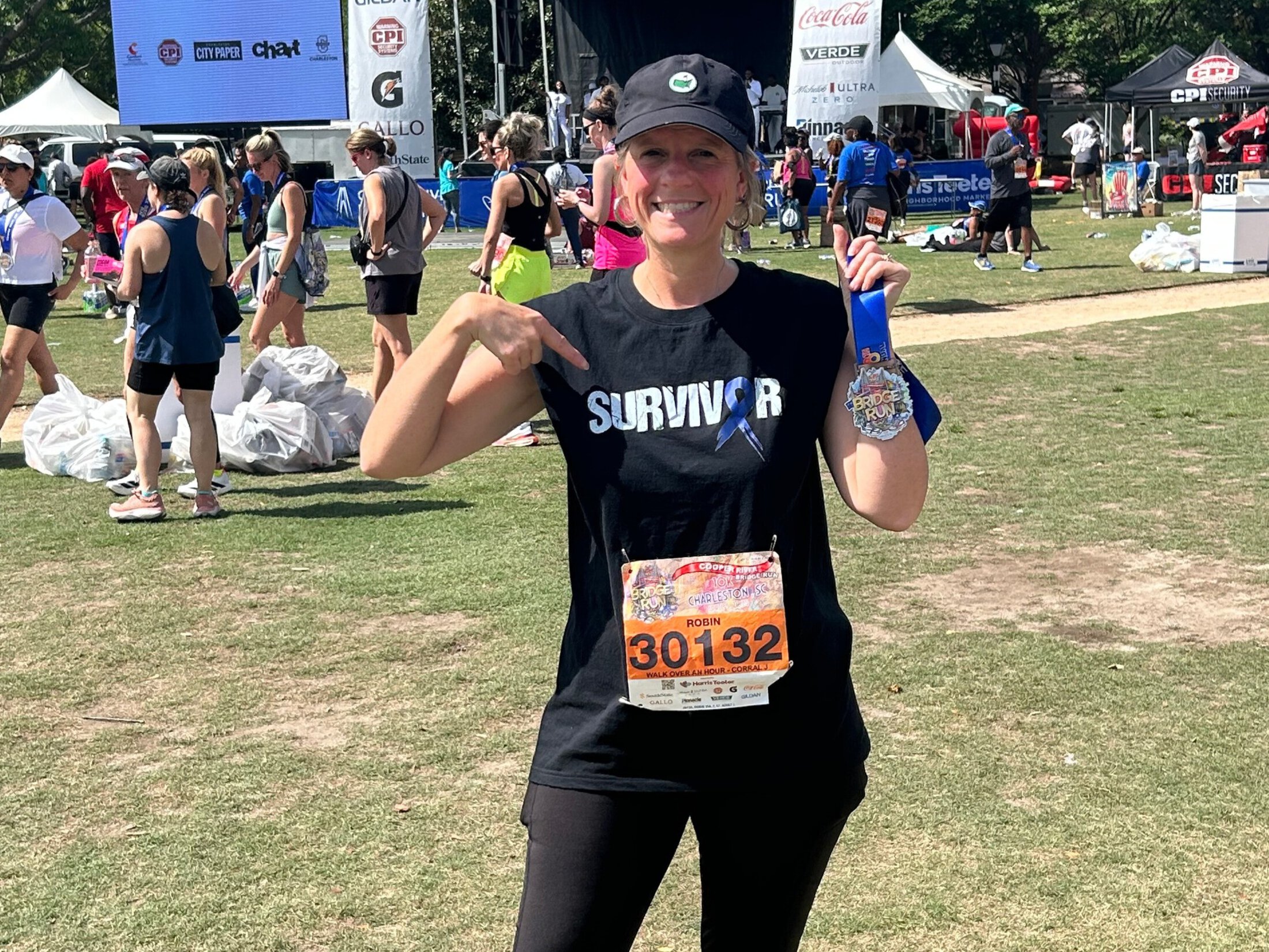 a woman holds up a 10K medal and points to the word 'survivor' on her T-shirt