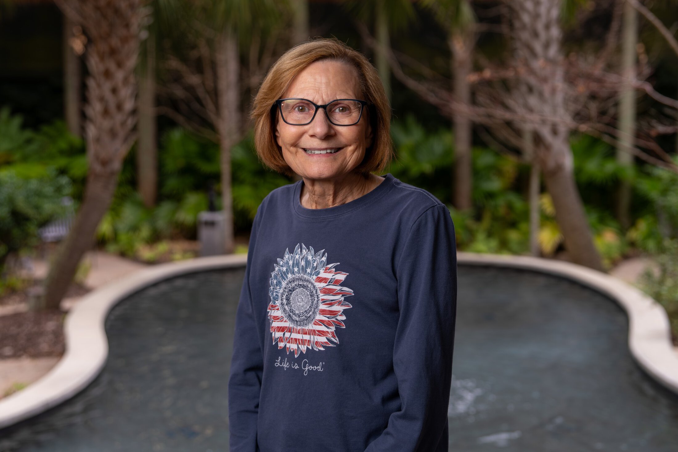 A woman poses in a garden setting.