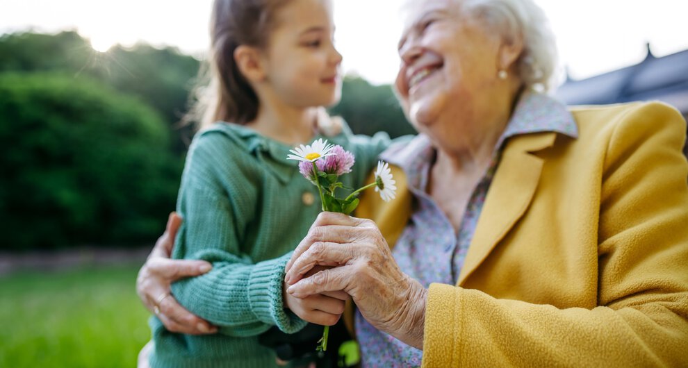 Granddaughter spending time with elderly grandma, picking wildflowers. Senior lady spending time in nature.