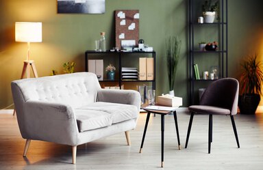 An empty sofa and an empty chair with a table between them. There is soft lighting and a box of tissue and a glass on the table.
