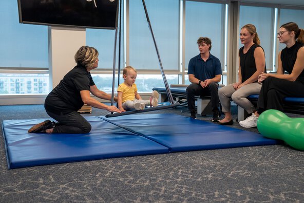 woman demonstrates pushing toddler on swing in front of college students as demonstration