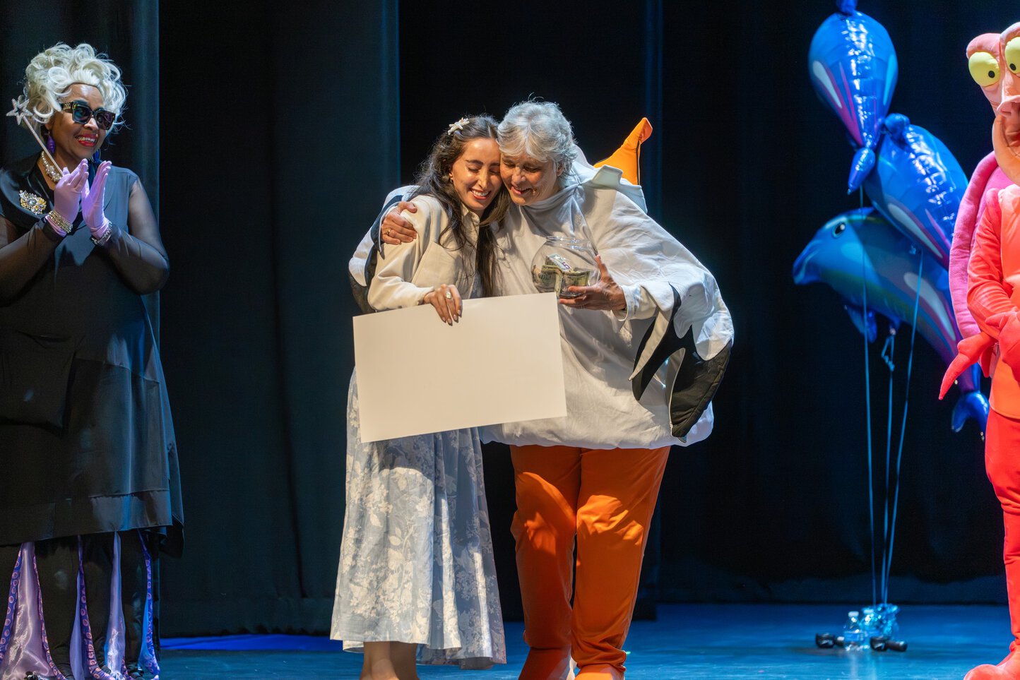 Faculty members dressed as characters from the Little Mermaid stand on stage as a woman dressed as a fish hugs a smiling medical students.