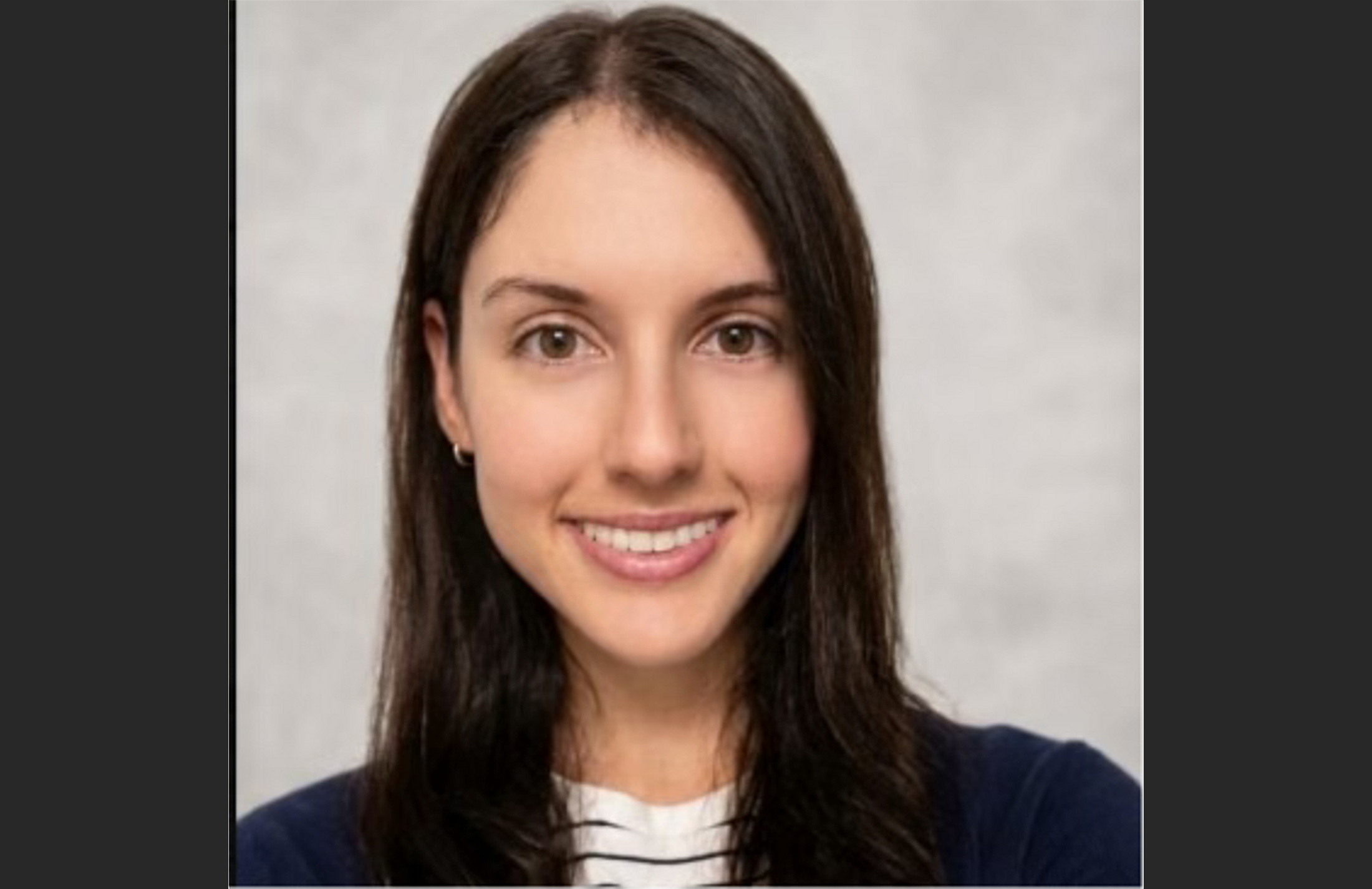 Headshot of young woman with long dark hair. She is smiling and wearing a white striped shirt and blue jacket.