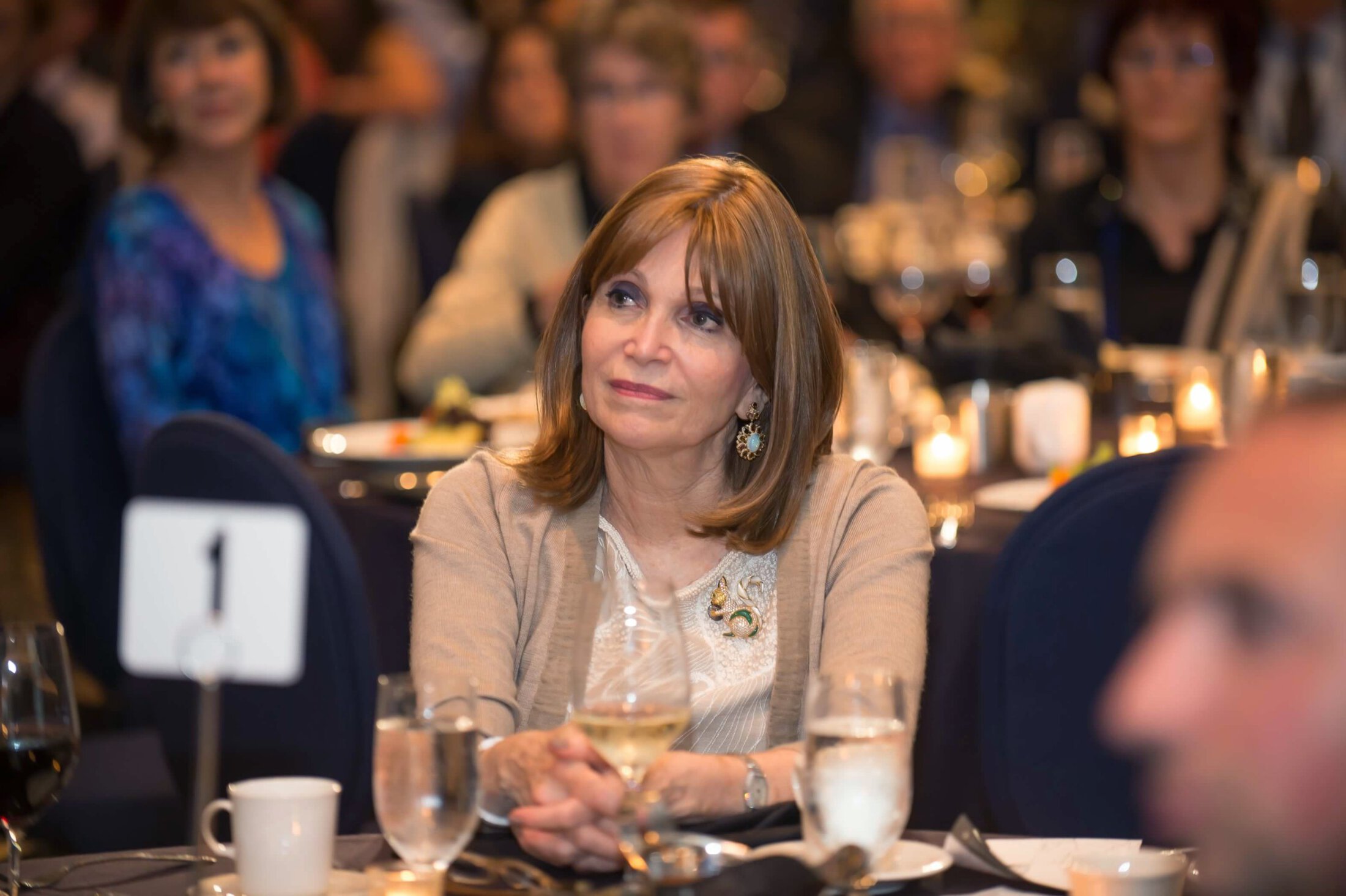 A woman in formal attire sits at a table during a dinner reception.