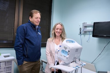 Dr. Sarah Miller, College of Nursing, and Dr. Charlie Strange, College of Medicine, stand in a clinical exam room reviewing simulated patient readings on a portable respiratory monitoring device used in chronic obstructive pulmonary disease (COPD) research, with medical equipment visible in the background.