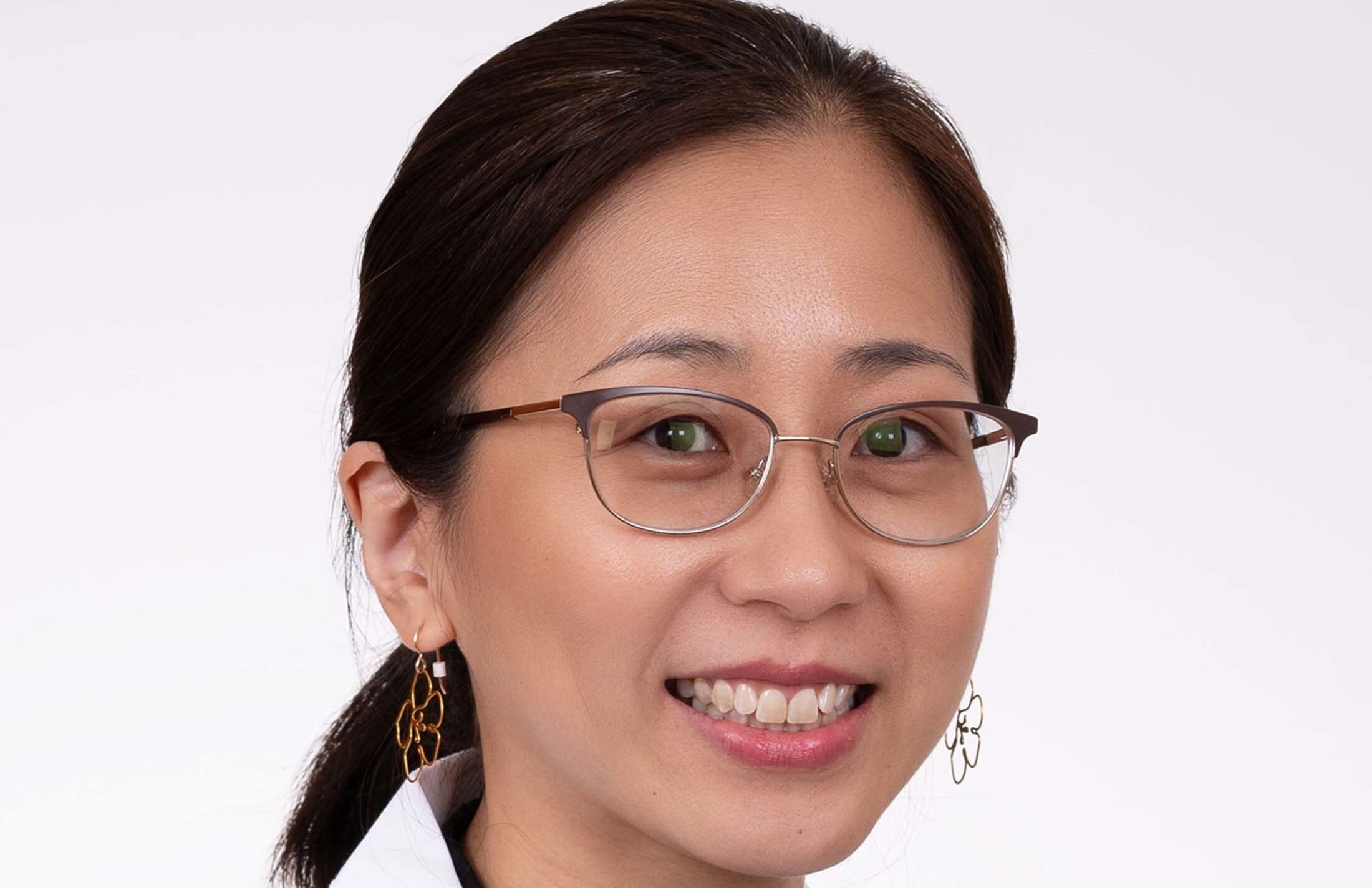 Headshot of woman with long dark hair. She is wearing eye glasses and dangly earrings with flowers on them.