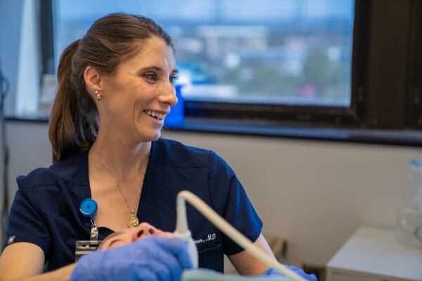 A physician looks at a screen as she holds a radiofrequency device up to a patient's neck.