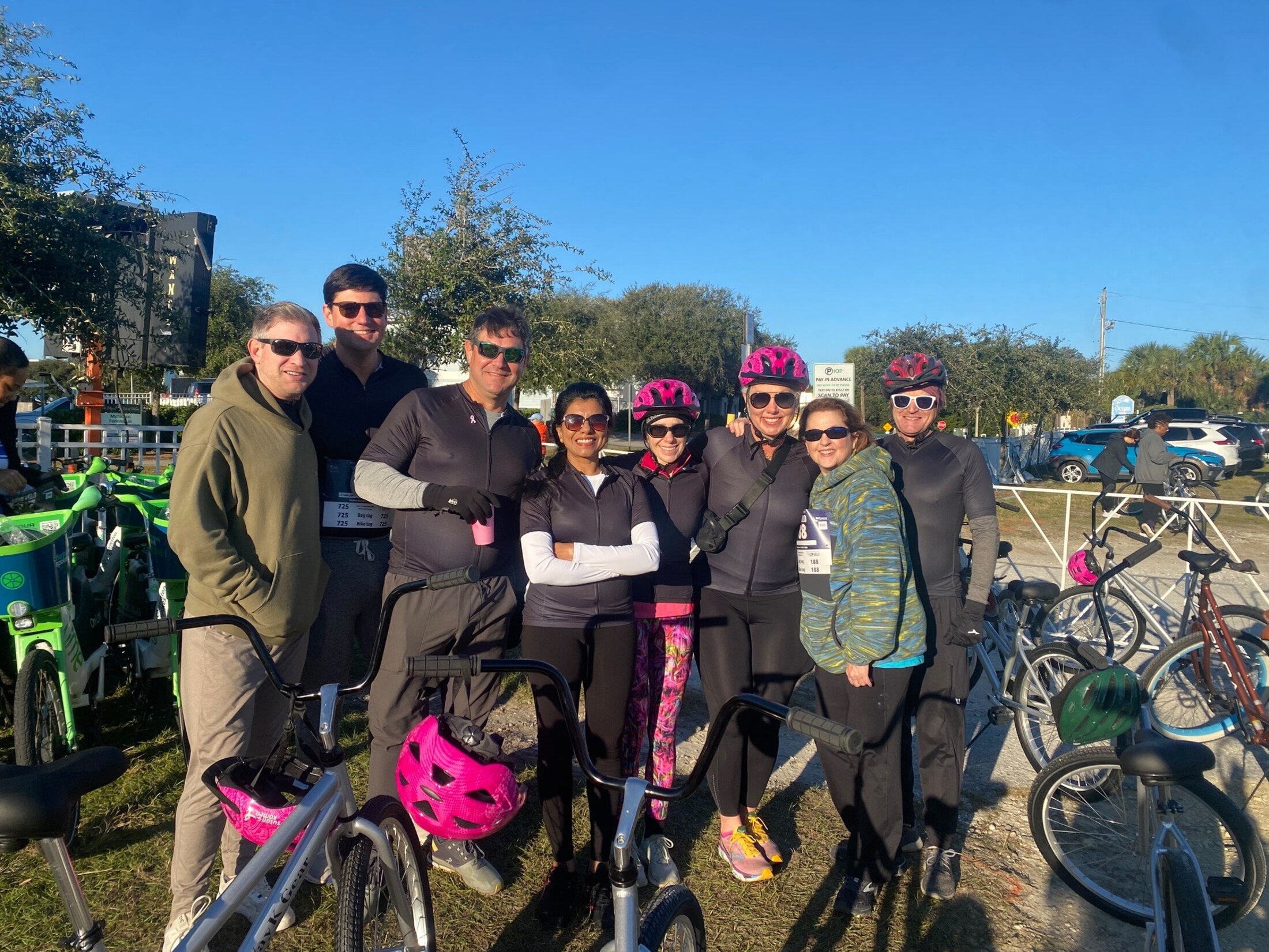 A group of people in bicycling gear pose amidst parked bicycles.