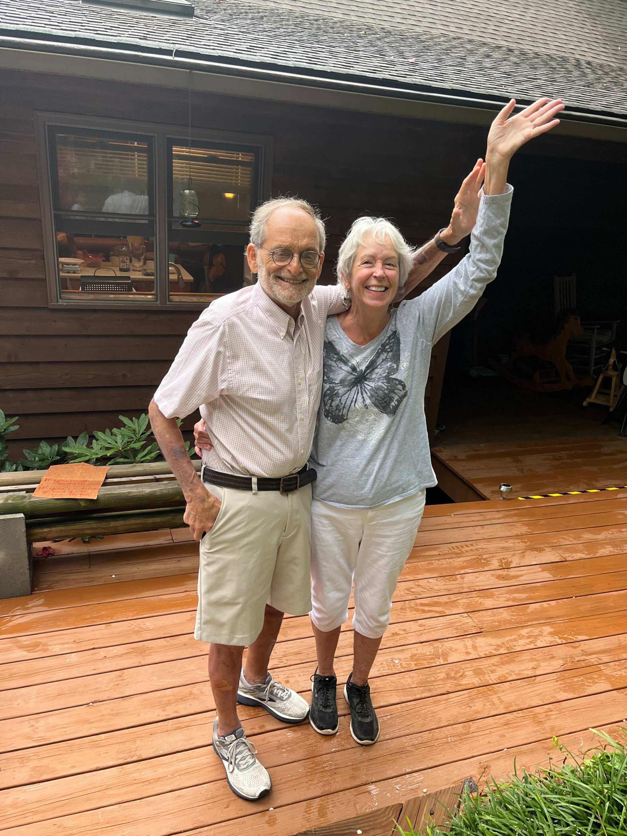 An older couple wave from a patio.