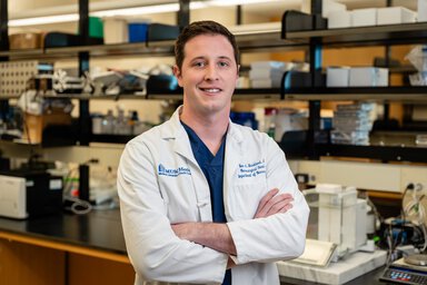 A portrait of a male cancer researcher wearing a white coat in a lab.