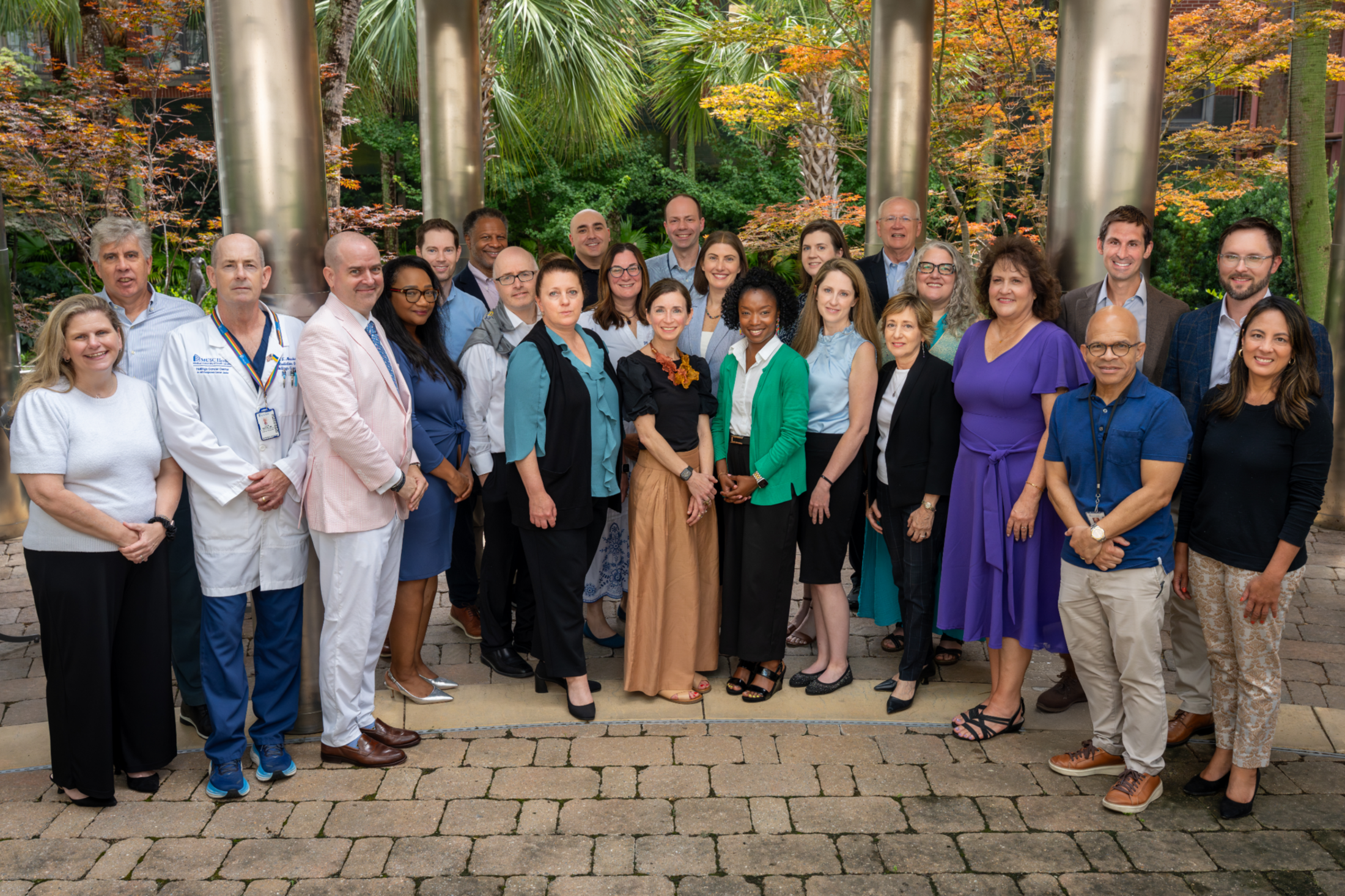 A large group of early career and established faculty and staff pose together in a garden.