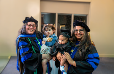 two women holding children pose in their regalia for graduation