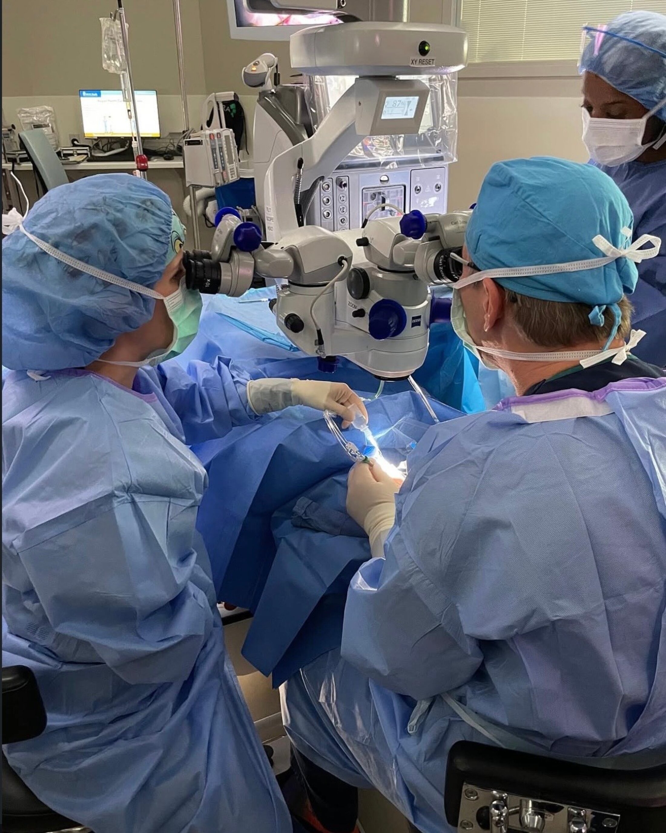 Three people in blue scrubs surround medical equipment and a patient under a blue blanket.