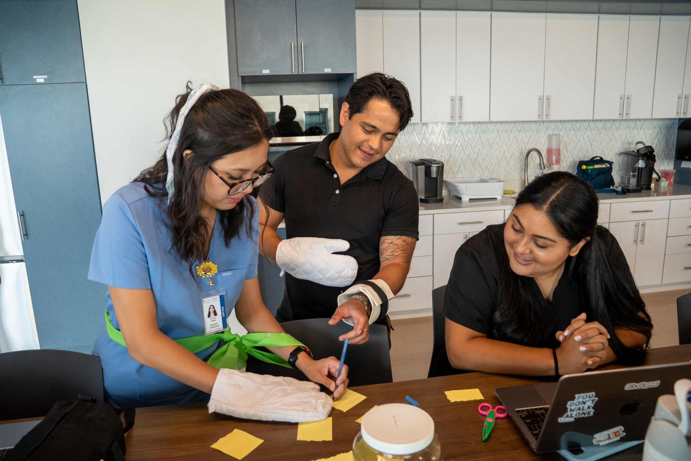 Three students work together in a simulated kitchen, practicing cooking and daily living skills during an OT lab immersion.
