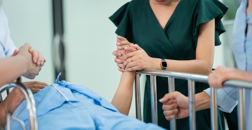 woman gently holds a patient's hand in a hospital, showcasing care and compassion. Relatives stand to give encouragement to a patient lying on a hospital bed. Relatives' encouragement of patients