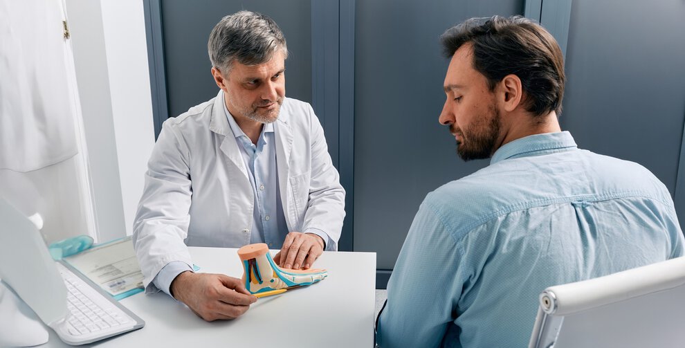Flat feet treatment. Podiatrist doctor consulting adult man with flatfoot, explaining treatment methods using anatomical pes planus model