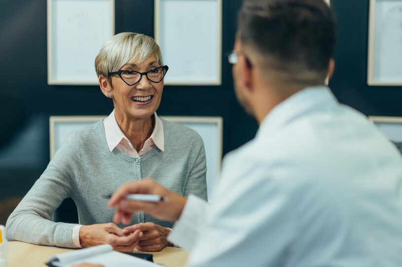 A woman smiles as she listens to a medical professional across the table from her.