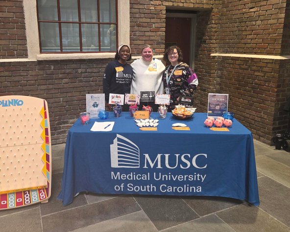 An MUSC table display with informational materials, giveaways, and a large Plinko board, with three people standing behind the table.