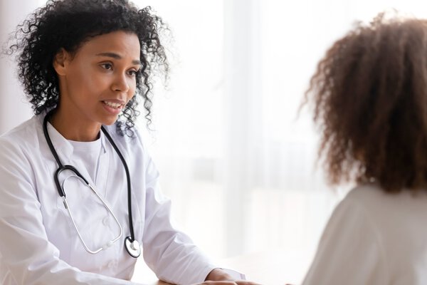 Smiling African American doctor in white uniform with stethoscope talking to patient