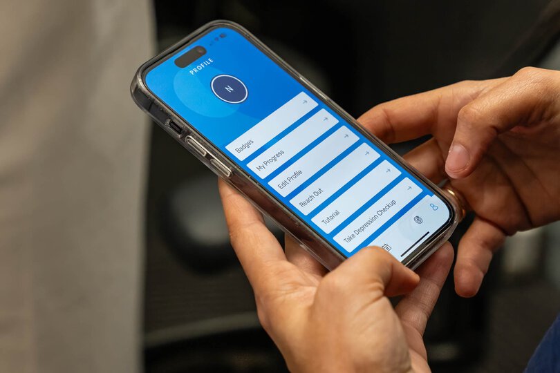 A close up of hands holding a mobile phone with a mental health app open on the screen.