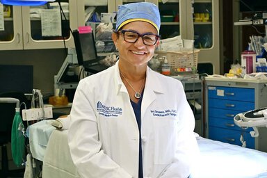 Dr. Smolens, smiling wearing a lab coat inside a hospital room with a hospital bed