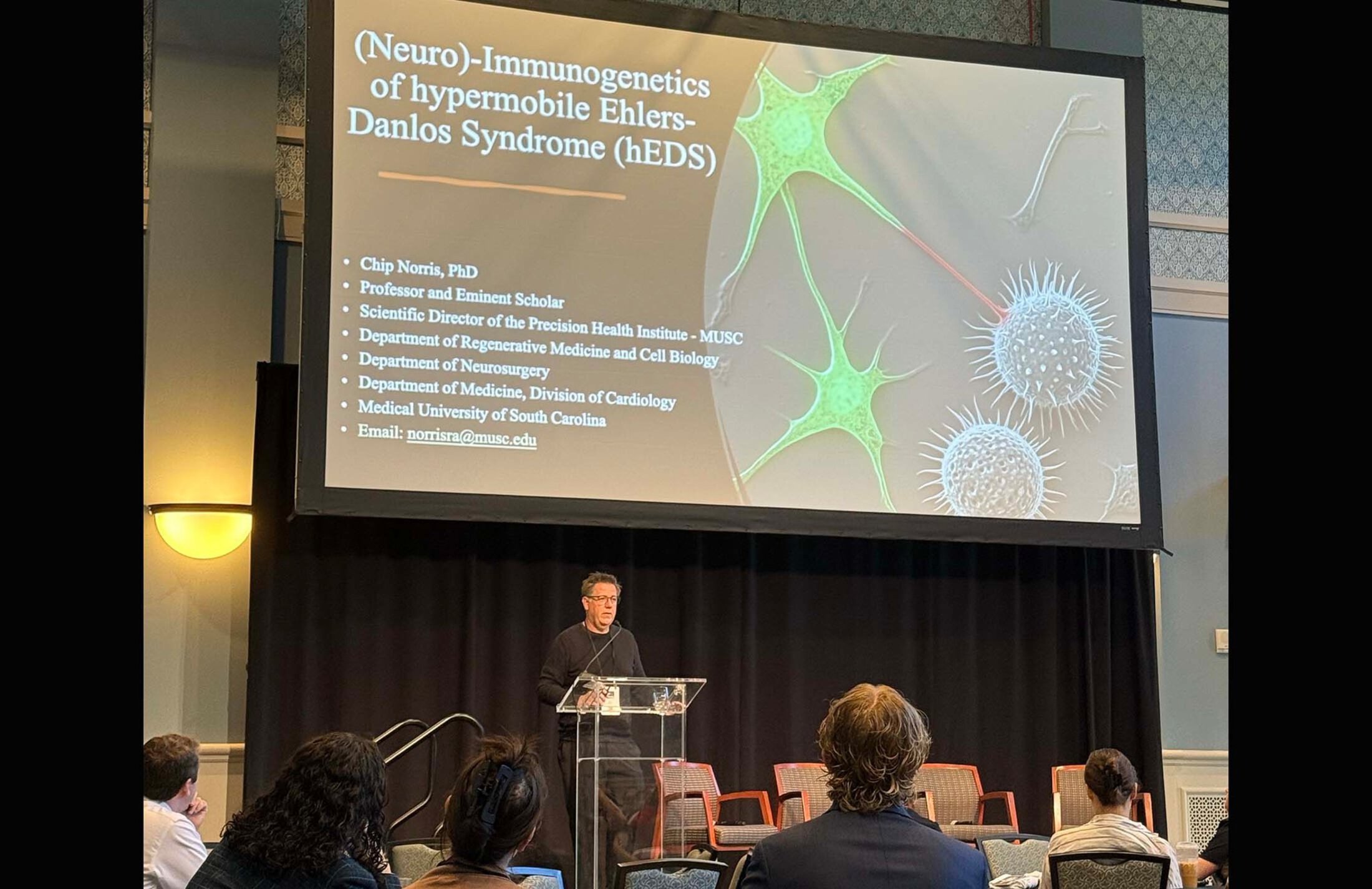 Man at a podium under a screen that says Neuro-Immunogenetics of hypermobile Ehlers-Danlos Syndrome. Chip Norris, Ph.D. Lists his departments and his email address, which is norrisra@musc.edu