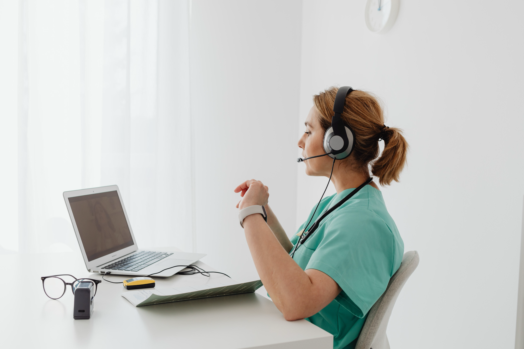 woman in scrubs seated with headset on and looking at laptop