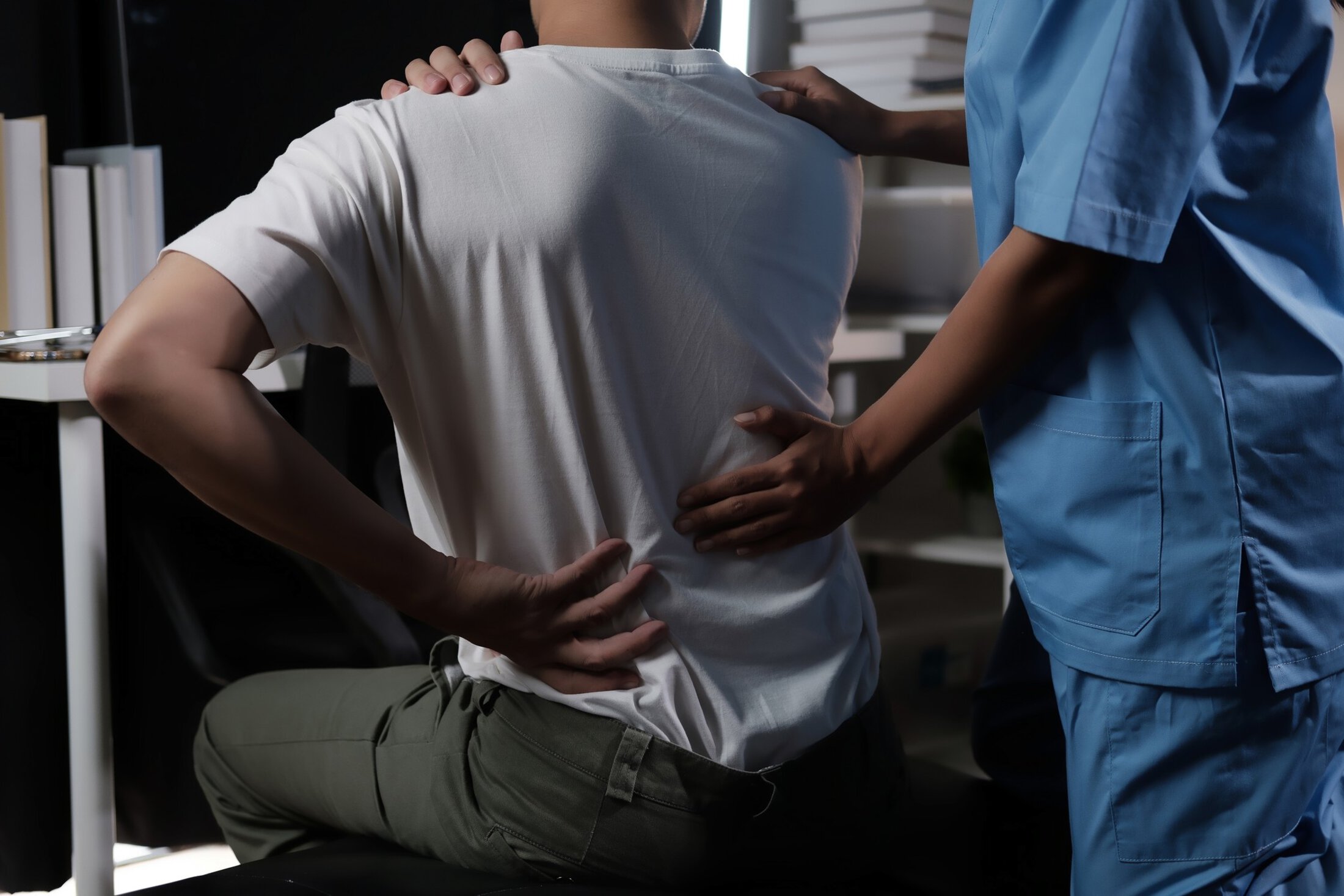 A man with a back injury is being helped by a nurse. The nurse is wearing a blue uniform