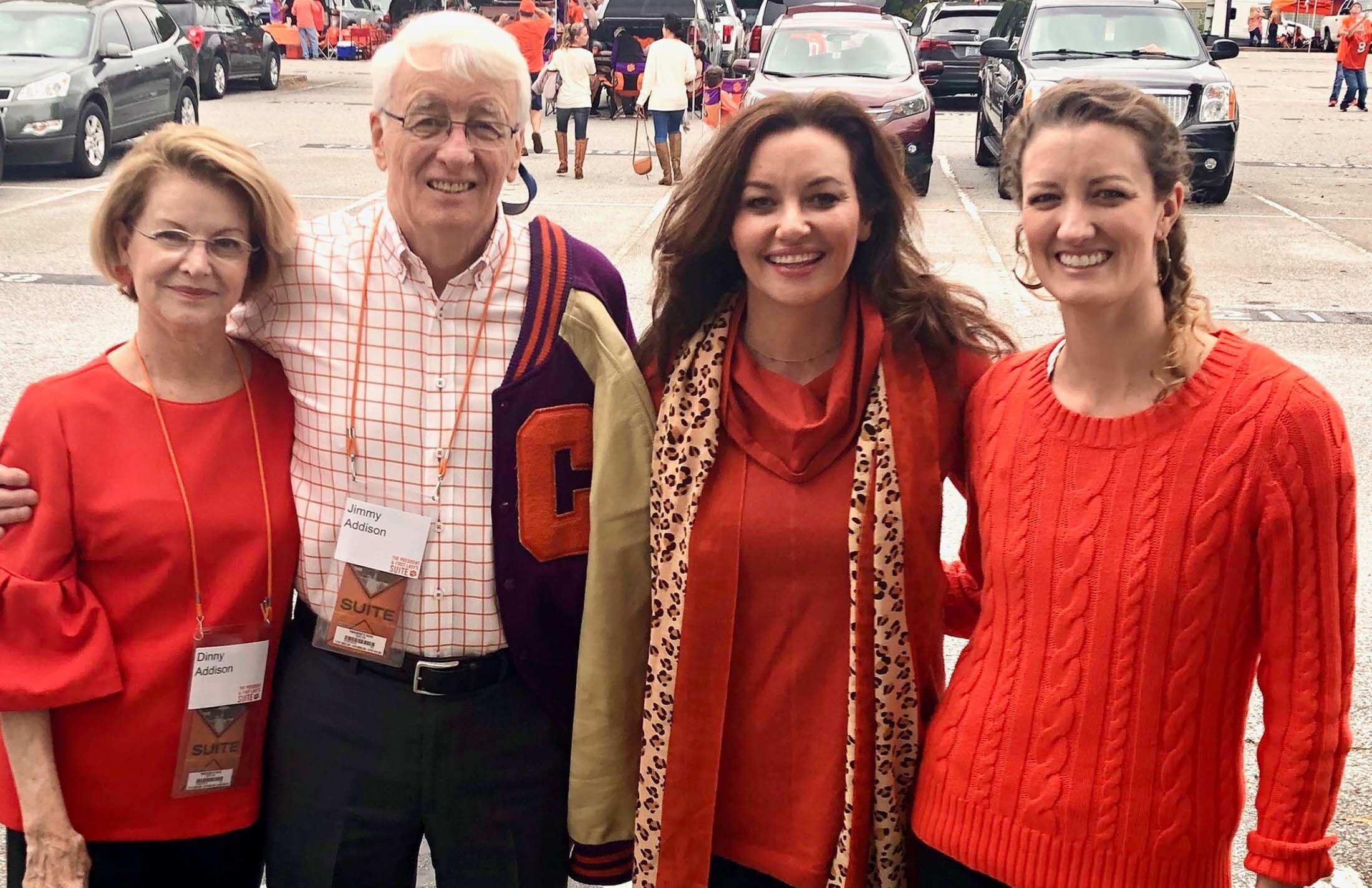 A family of four stands in a parking lot at what appears to be a tailgating event. The man is wearing a Clemson jacket. His wife and two daughters are wearing Clemson orange.