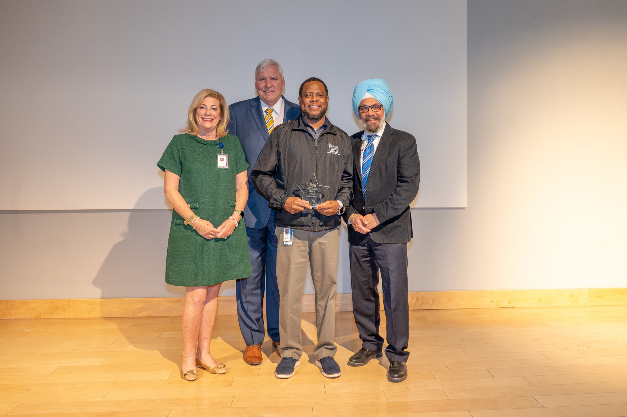 VIA AJ Johnson with Coles and Huja, Dr Cole and Mrs Cole standing on a stage giving award