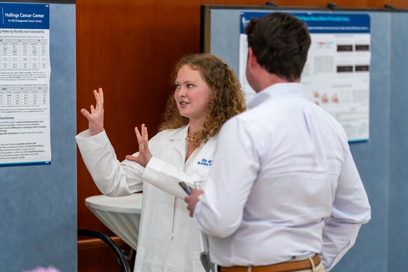 A student gestures toward her poster as she speaks to someone about her research.