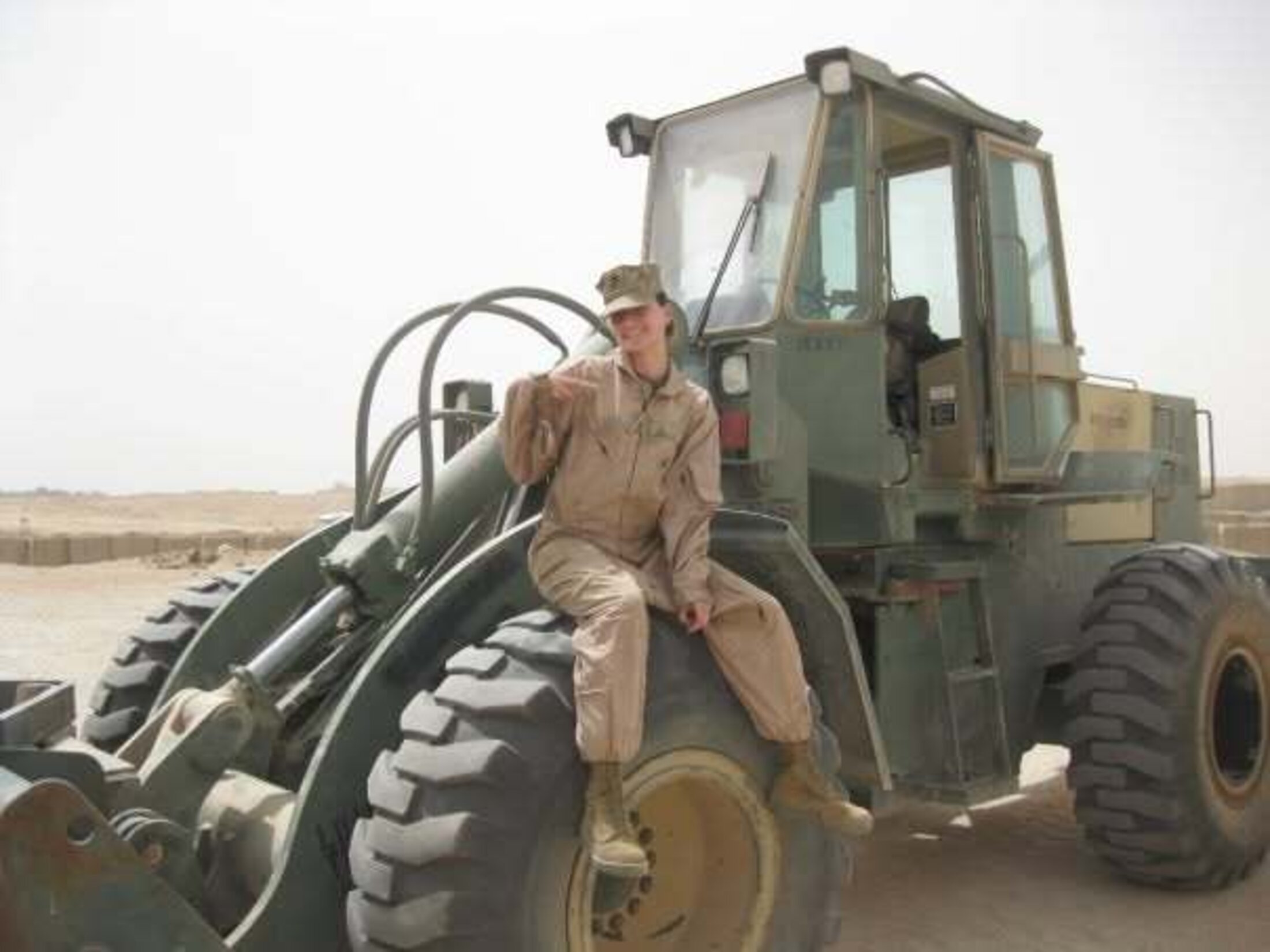 Woman sitting on military equipment. She is wearing a brown uniform with a cap.