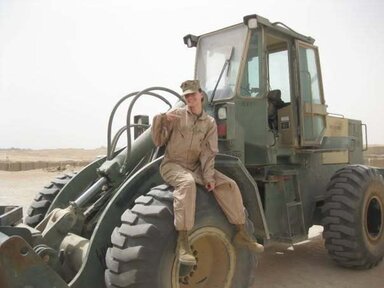 Woman sitting on military equipment. She is wearing a brown uniform with a cap.