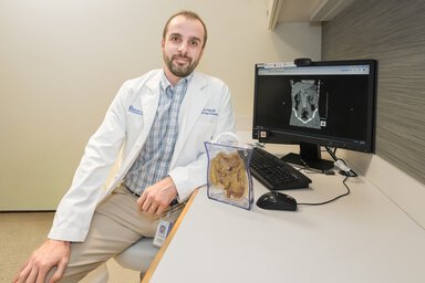 Gregory Habig, MD wearing a white coat sitting in front of a computer screen.