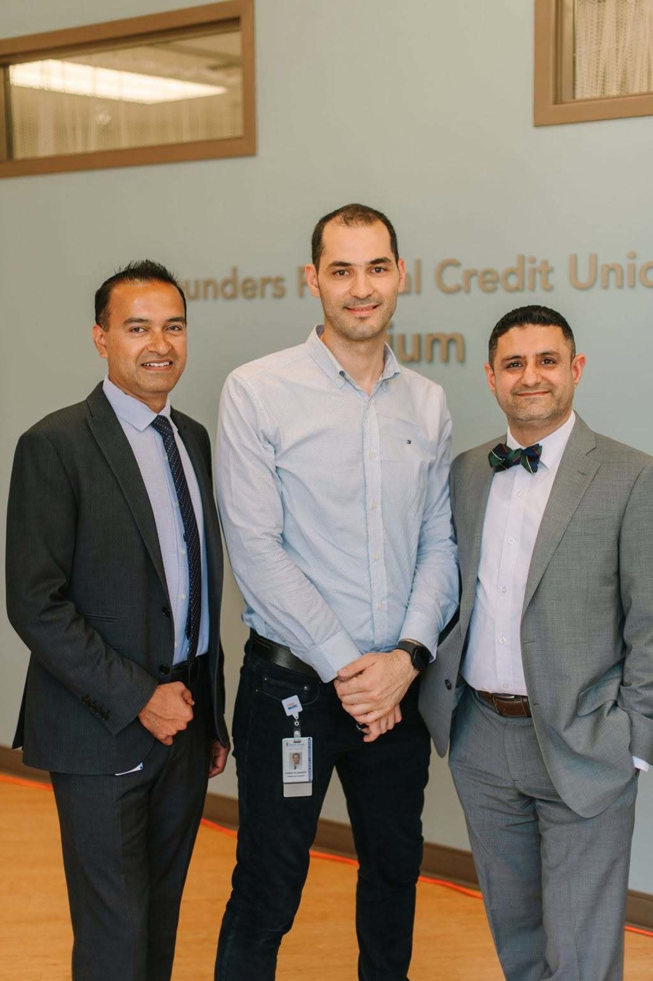Three men wearing business attire stand in a hallway with a blue wall behind them and the words Founders Credit Union